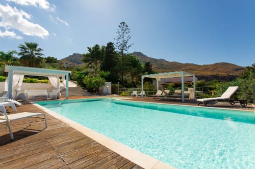 Turquoise pool with wooden deck, lounge chairs, pergolas, and mountain views at Villa Maria, Sant'Andrea, Valderice