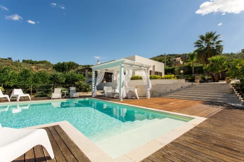 Luxury villa pool with turquoise water, wooden deck, cabana, and Mediterranean hillside views in Sant'Andrea, Sicily