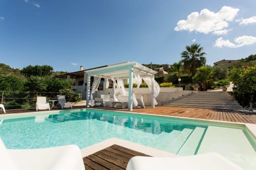 Luxury villa pool with turquoise water, pergola, wooden deck, and palm trees in Sant'Andrea, Valderice, Italy