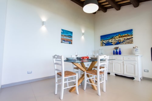 Modern dining room with white chairs, wooden table, coastal artwork, and Mediterranean décor at Villa Maria