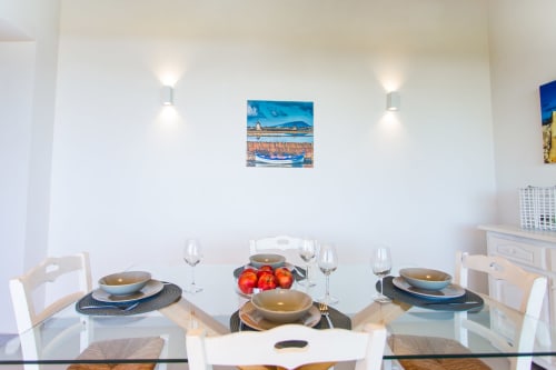 Modern dining area at Villa Maria with elegant table setting, blue boat artwork, and Mediterranean coastal view
