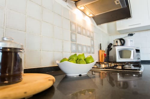Modern kitchen at Villa Maria with green pears in white bowl, stove, microwave, and tiled backsplash, Sant'Andrea