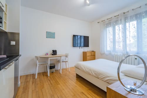 Studio moderne à Toulouse avec parquet, lit, bureau, TV et baies vitrées lumineuses avec vue sur la ville