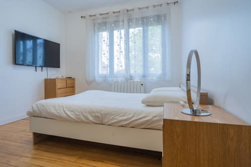 Chambre moderne à Room In Toulouse avec lit queen-size, téléviseur mural, commode en bois et grande fenêtre aux voilages
