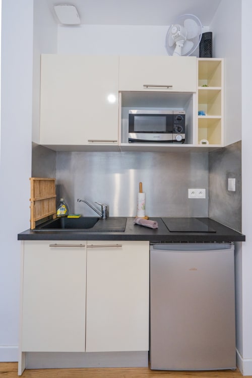 Petite cuisine à Toulouse avec plan de travail noir, placards blancs, micro-ondes et réfrigérateur inox