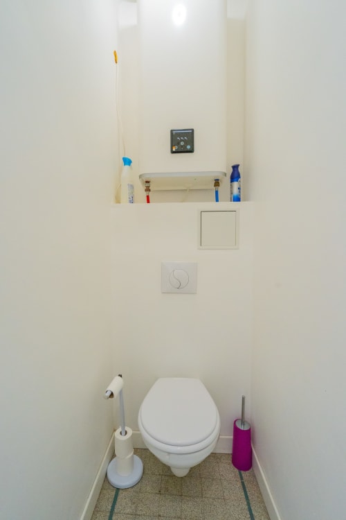 Toilettes immaculées avec abattant blanc, porte-rouleau, brosse et flacon de nettoyant bleu dans un appartement toulousain