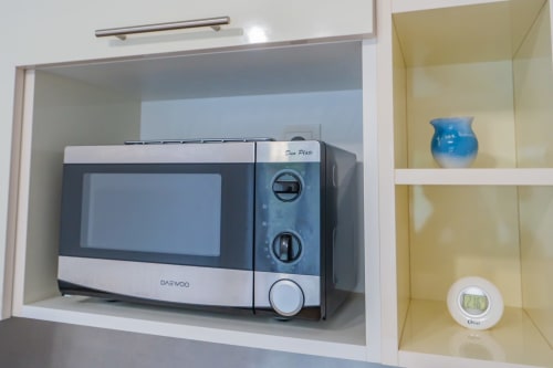 Micro-ondes Daewoo dans placard de cuisine à l'appartement Room In Toulouse avec vase bleu et thermomètre sur l'étagère