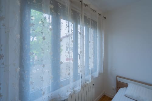 Chambre lumineuse avec rideaux fleuris transparents, lit en bois et vue sur la ville à l'appartement Room In Toulouse