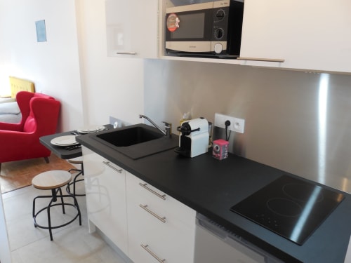 Cuisine moderne de l'appartement toulousain avec plan de travail noir, plaque induction, évier, micro-ondes et acier inoxydable