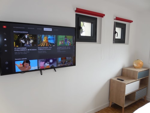 Chambre d'appartement moderne avec écran plat mural affichant du contenu en streaming, table de nuit en bois avec lampe, et