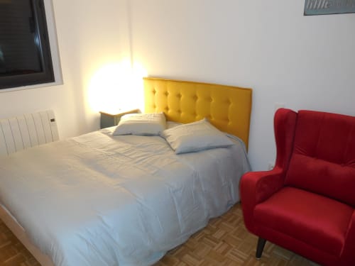 Chambre moderne lumineuse avec tête de lit jaune, literie blanche, fauteuil rouge et radiateur mural à l'hôtel Room In Toulouse