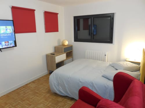 Chambre moderne à Room In Toulouse avec lit double, accents rouges, TV écran plat, mobilier en bois et vue sur la ville