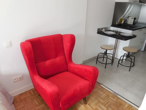 Fauteuil crapaud rouge dans un appartement toulousain avec kitchenette et coin bar en arrière-plan