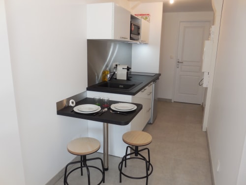 Petite cuisine moderne dans un appartement toulousain avec comptoir de repas, deux tabourets, plan de travail noir et inox