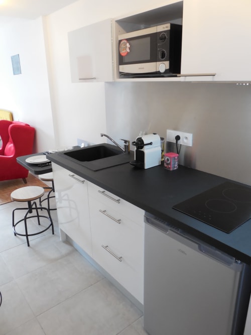 Petite cuisine moderne à Toulouse avec plan de travail noir, meubles blancs, cuisinière à induction, évier, micro-ondes et bar