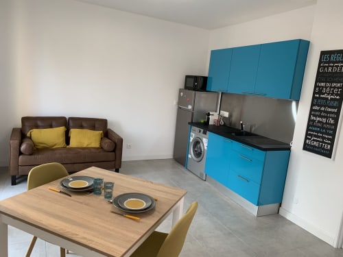 Studio moderne à Toulouse avec cuisine bleue, canapé marron, table à manger et lave-linge