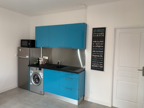 Cuisine moderne avec meubles turquoise, plan de travail noir, lave-linge et électroménagers inox à Toulouse