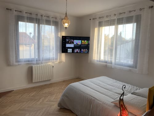 Chambre lumineuse à Toulouse avec lit double, TV écran plat, rideaux voilages, radiateur et accès à balcon avec vue sur la ville.
