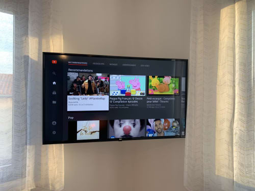 Recommandations YouTube affichées sur téléviseur écran plat dans un appartement à Toulouse avec vue sur la ville et rideaux voilages