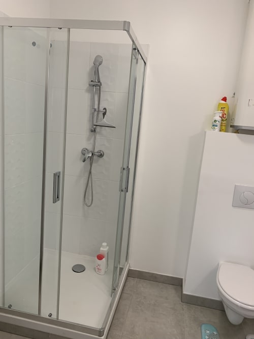 Cabine de douche moderne en verre dans la salle de bains d'un appartement toulousain avec robinetterie chromée et carrelage blanc