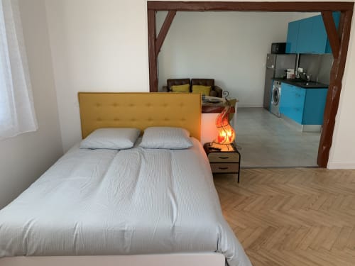Petit studio moderne à Toulouse avec lit à tête de lit jaune, kitchenette aux placards bleus et parquet en chevrons