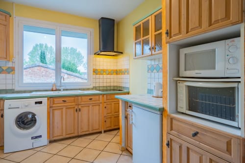Cuisine jaune éclatante avec meubles en bois, plan de travail turquoise, lave-linge, four et vue sur fenêtre à Toulouse