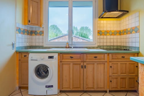 Cuisine moderne avec lave-linge, meubles en bois et carrelage jaune donnant sur les arbres dans un appartement à Toulouse