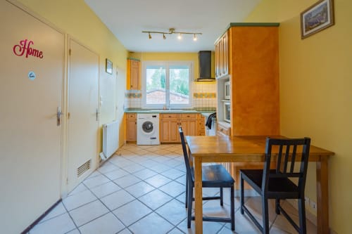 Cuisine-séjour lumineux en jaune vif dans un appartement toulousain, table en bois, placards orange et électroménagers modernes