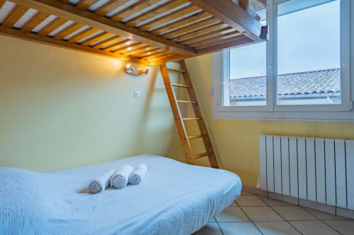 Chambre loft moderne à Toulouse avec lit mezzanine, échelle en bois, radiateur et vue sur la ville