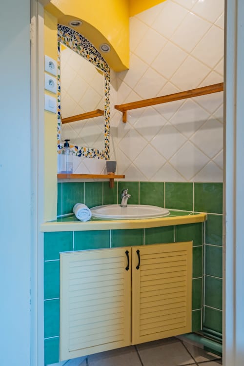 Salle de bain moderne avec carrelage jaune et vert, meuble vasque en bois, lavabo rond et miroir décoratif à l'appartement Room In Toulouse