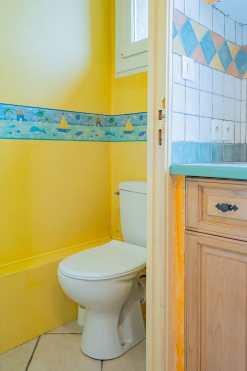 Salle de bains jaune vif avec frise murale à thème océan coloré et toilettes blanches dans un appartement toulousain