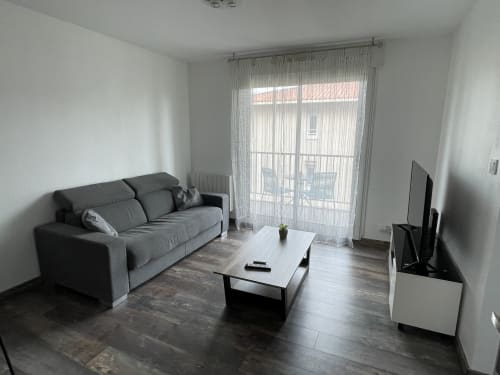 Séjour moderne à Toulouse avec canapé gris, TV écran plat et accès à un balcon vue sur la piscine.