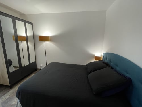 Chambre moderne à Room In Toulouse avec literie noire, tête de lit bleue, armoire miroir et appliques en laiton à La