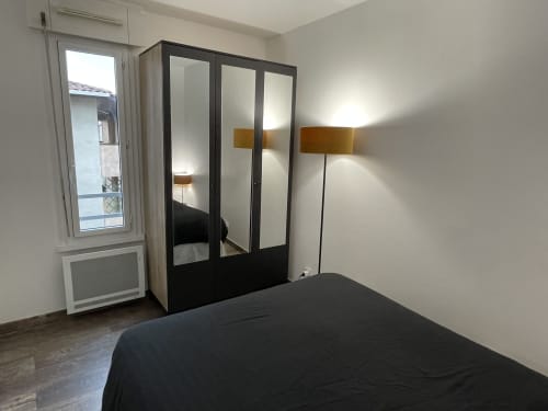 Chambre moderne dans un appartement toulousain avec armoire miroir, lit, appliques murales et porte-fenêtre