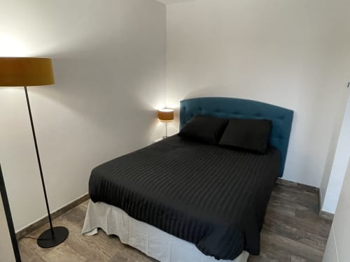 Chambre moderne dans un appartement toulousain avec tête de lit bleue, literie noire, lampadaire et applique murale