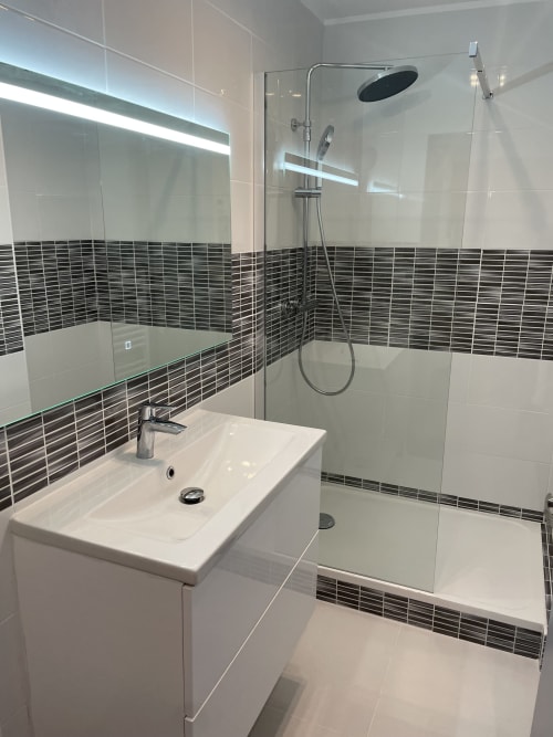 Salle de bain moderne avec lavabo blanc, pluie de douche, frise carrelage foncé et cabine douche vitrée au Room In Toulouse
