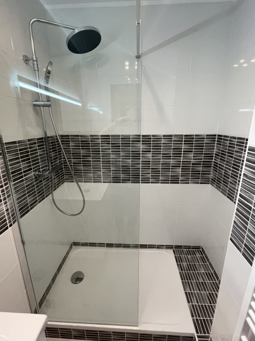 Douche moderne avec carrelage linéaire noir, pommeau de douche pluie et paroi en verre dans appartement toulousain