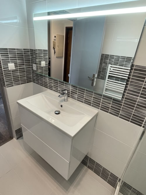 Vanité de salle de bain moderne avec meuble lavabo blanc, dosseret en carrelage gris rayé et miroir rétroéclairé à Room In Toulouse