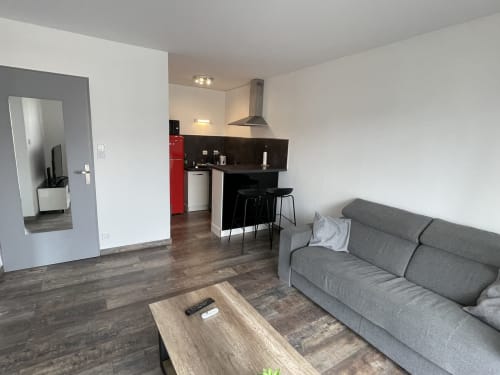 Salon moderne d'un appartement à Toulouse avec canapé gris, cuisine et coin bar avec sièges noirs