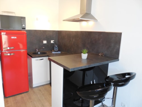 Cuisine moderne avec réfrigérateur SABA rouge, plan de travail foncé, hotte inox et bar noir à Toulouse