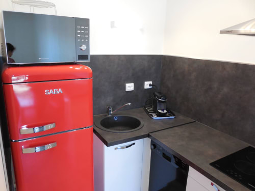 Petite cuisine de l'appartement toulousain avec réfrigérateur SABA rouge, micro-ondes, évier et plaque de cuisson électrique