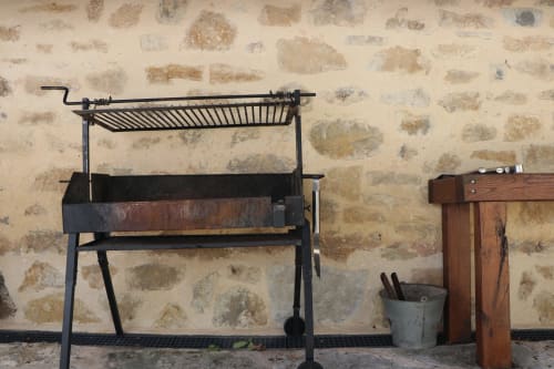Parrilla tradicional de hierro para barbacoa contra pared de piedra rústica en Casa Lafuente, Lukiano, España.