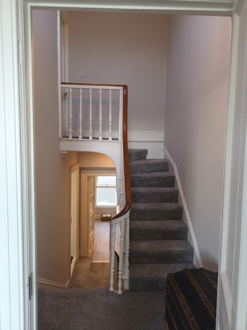 Staircase and landing at Eglinton Road Bray B&B showing gray carpeted stairs with white railings and wooden bannister