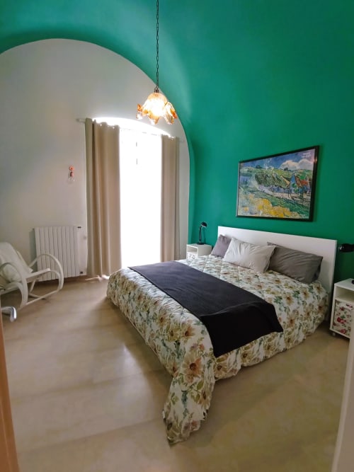 Camera luminosa della villa vacanze a Bari con pareti turchesi, biancheria floreale, lampada a sospensione e opere d'arte incorniciate