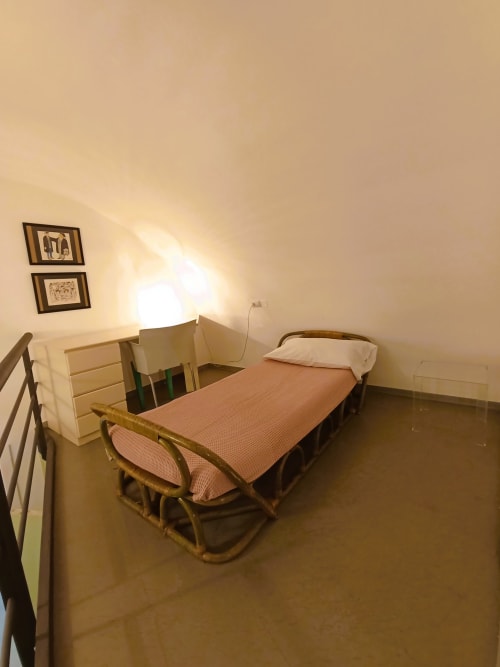 Camera da letto minimalista della villa a Bari con letto singolo, scrivania e quadri incorniciati su pareti color crema