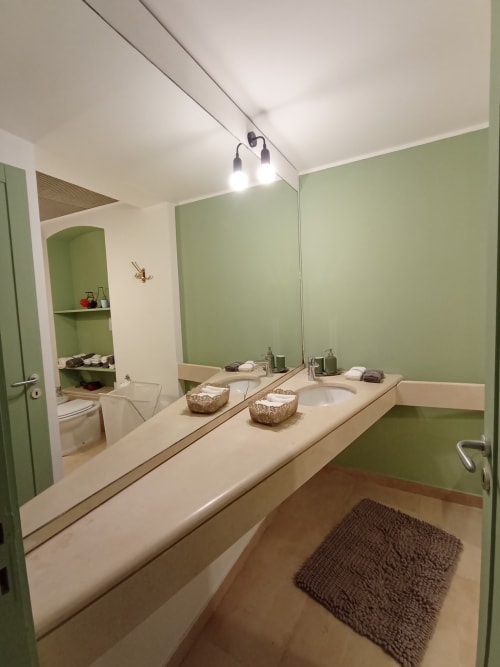 Bagno moderno della villa vacanze di Bari con pareti verdi, doppio lavabo, specchio grande e tappetino marrone
