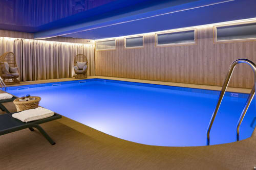 Indoor swimming pool at Hotel Residence Europe & Spa in Clichy with blue water, lounge chairs, and modern lighting
