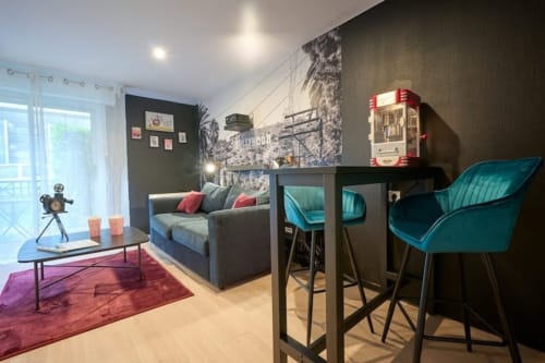 Cinema-themed apartment studio in Bordeaux with turquoise chairs, gray sofa, and Hollywood sign wall decor