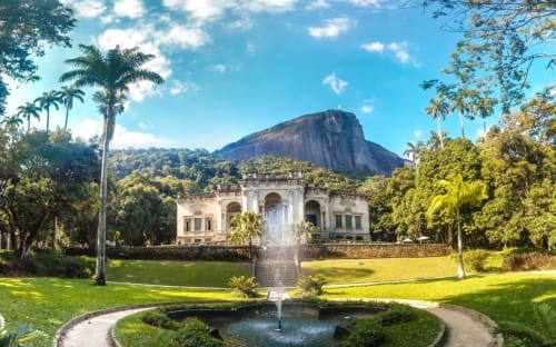 Mansão histórica com fonte em jardins exuberantes, com vista do Rio de Janeiro e pico de montanha ao fundo