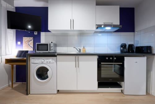 Modern kitchen in Bordeaux apartment with white cabinets, washing machine, oven, and dark blue accent wall
